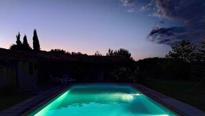 A rectangular swimming pool with a tiled edge, surrounded by a low brick wall. There are lounge chairs along the wall, and the pool is illuminated with a green light.