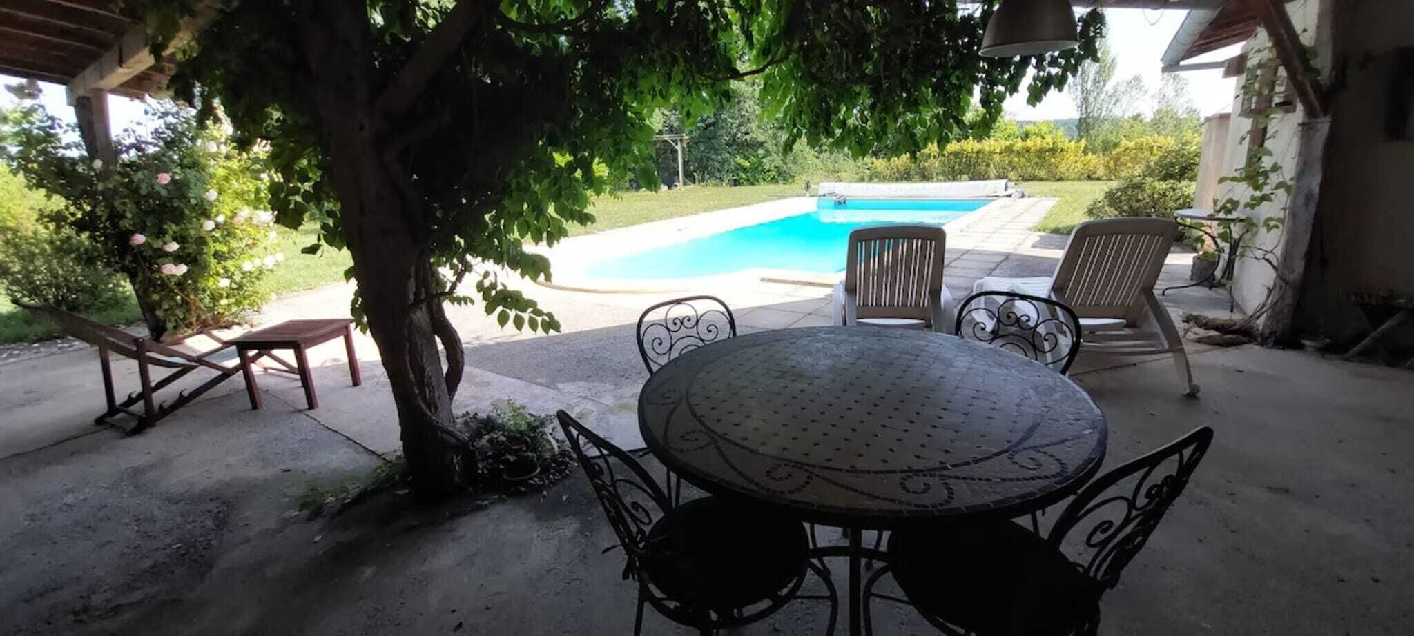 Eine Terrasse im Freien mit einem runden Tisch und Stühlen, einem kleinen Pool und einem Baum, der Schatten spendet.