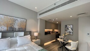 A modern hotel room with a large bed, a dining area, and a kitchenette.