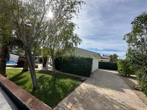 Un sendero pavimentado que conduce a un edificio blanco con techo rojo, rodeado de setos y árboles bien cuidados.