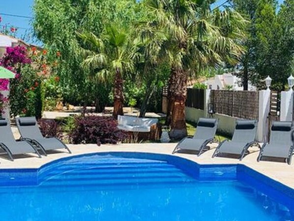 Una piscina con sillas de descanso y plantas tropicales.