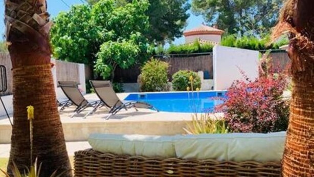 Un espace piscine avec des chaises longues, un canapé en osier et un palmier.