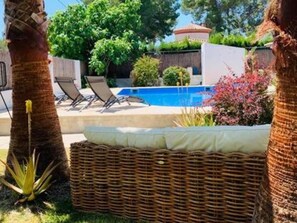 Un espace piscine avec des chaises longues, un canapé en osier et un palmier.