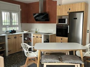 Una cocina compacta con encimera blanca, armarios de madera, microondas integrado y refrigerador de acero inoxidable.