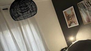 Une chambre à coucher avec un lit, un luminaire noir suspendu au plafond, une chaise et deux tableaux encadrés accrochés au mur.