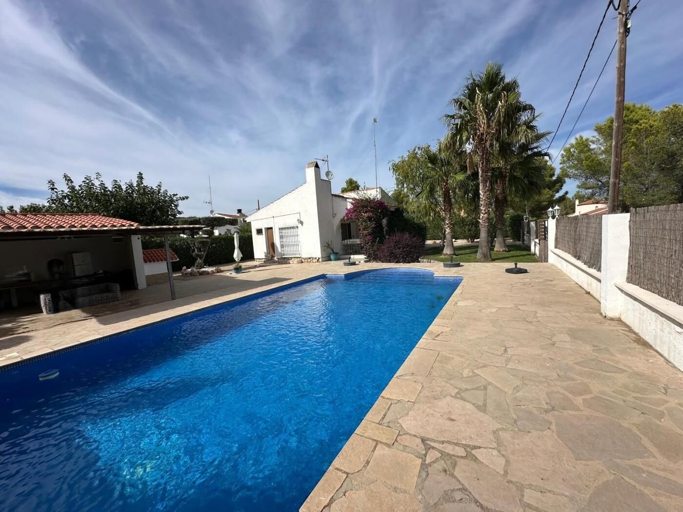 Una piscina amb rajoles de pedra, envoltada d'un edifici blanc i palmeres.