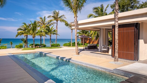 Een modern resort met een zwembad, palmbomen en uitzicht op de oceaan.