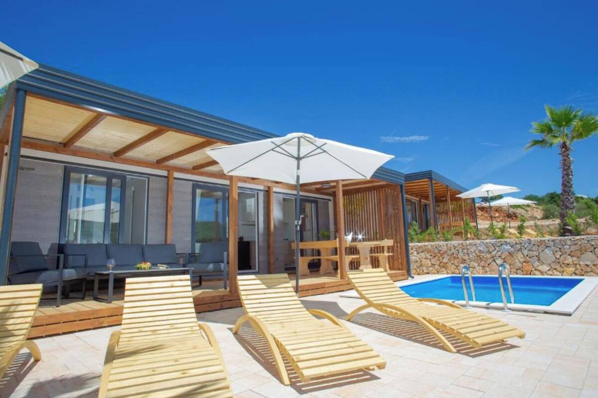 Ein moderner Poolbereich im Freien mit Holzliegen, einer überdachten Sitzgelegenheit und blauem Himmel.
