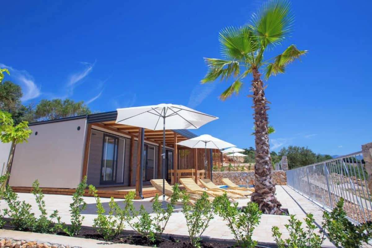 Eine moderne Villa mit Pool, Holzterrasse und Palmen.
