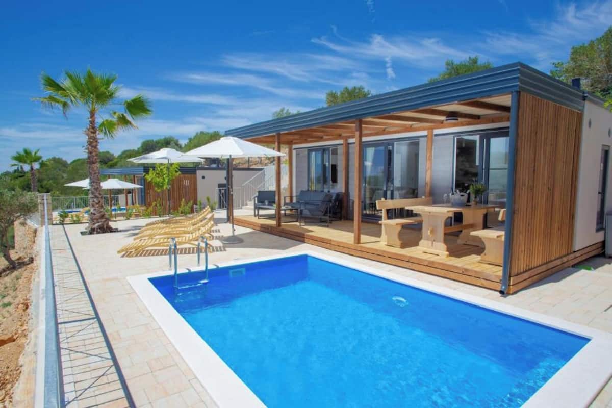 Ein modernes Haus mit Schwimmbad, Sitzgelegenheiten im Freien und einer überdachten Terrasse.