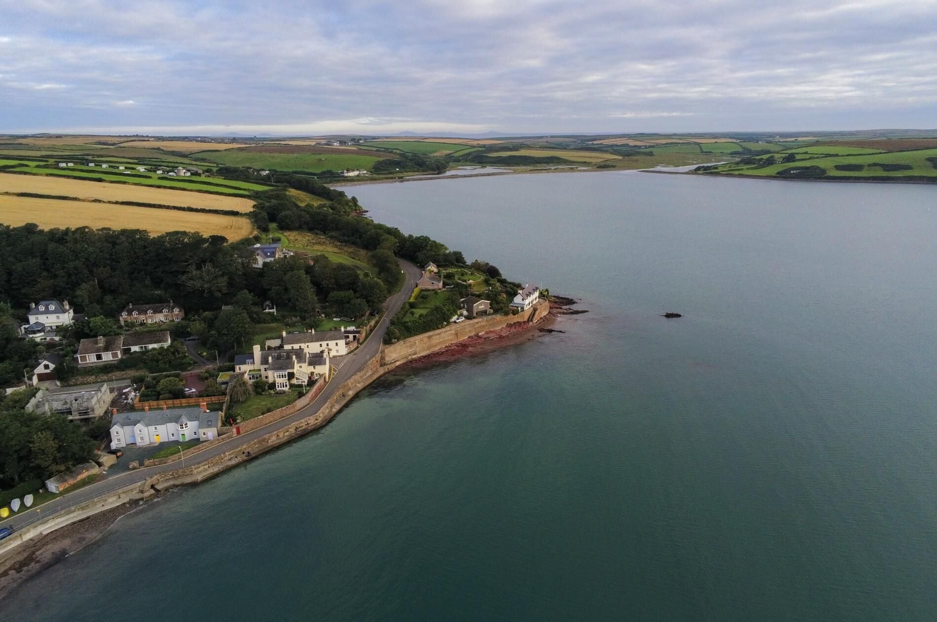 A coastal area with a road leading to a cluster of houses by the water.