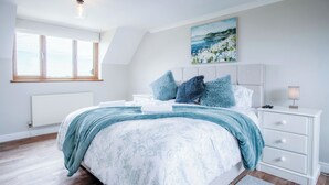 Une chambre à coucher avec un lit, une table de chevet, une lampe, un tableau et une fenêtre.
