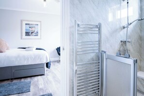 A modern bathroom with a shower, a glass door, and a marble wall. - Highfield - 5 Bedroom Holiday Home - Pembroke Dock (Pembroke Dock)