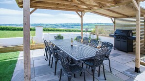Une terrasse extérieure dotée d’une structure en bois couverte, d’une table avec des chaises et d’un barbecue.
