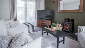 A modern living room with a sofa, a TV, a fireplace, and a large mirror. - Sunderland Avenue - 2 Bedroom - Pembroke Dock (Pembroke Dock)