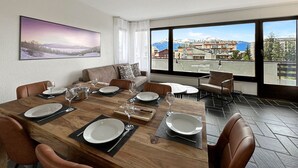 Un coin repas avec une table en bois dressée pour quatre personnes, un canapé et une grande fenêtre donnant sur les montagnes.