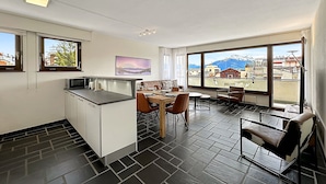 Une cuisine moderne avec un coin repas, de grandes fenêtres offrant une vue sur les montagnes et un petit îlot central.
