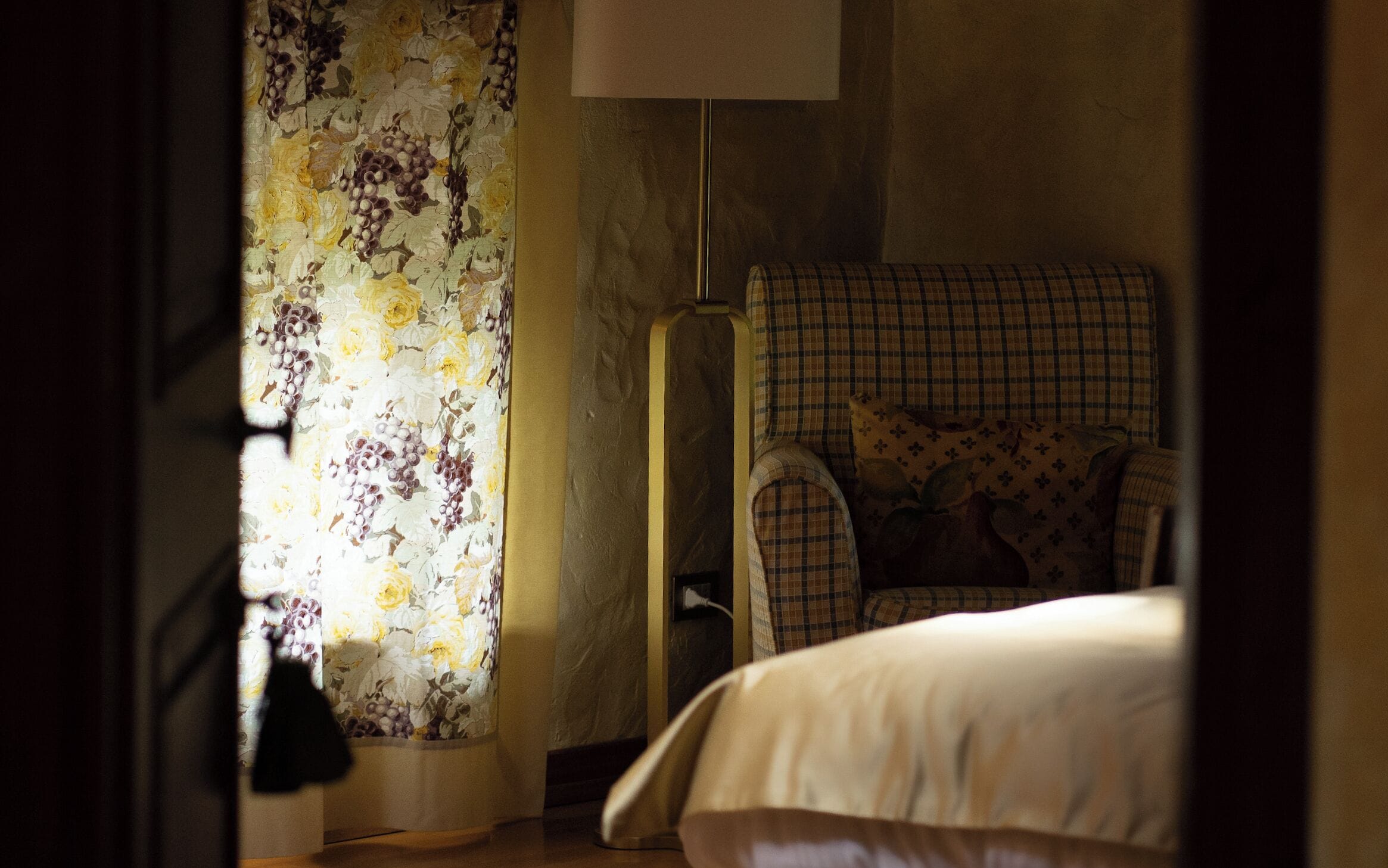 Un dormitorio con cama, lámpara y cortina estampada.