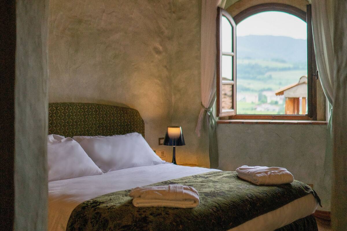 A bed with white linens, a green headboard, and a window with a view of buildings.