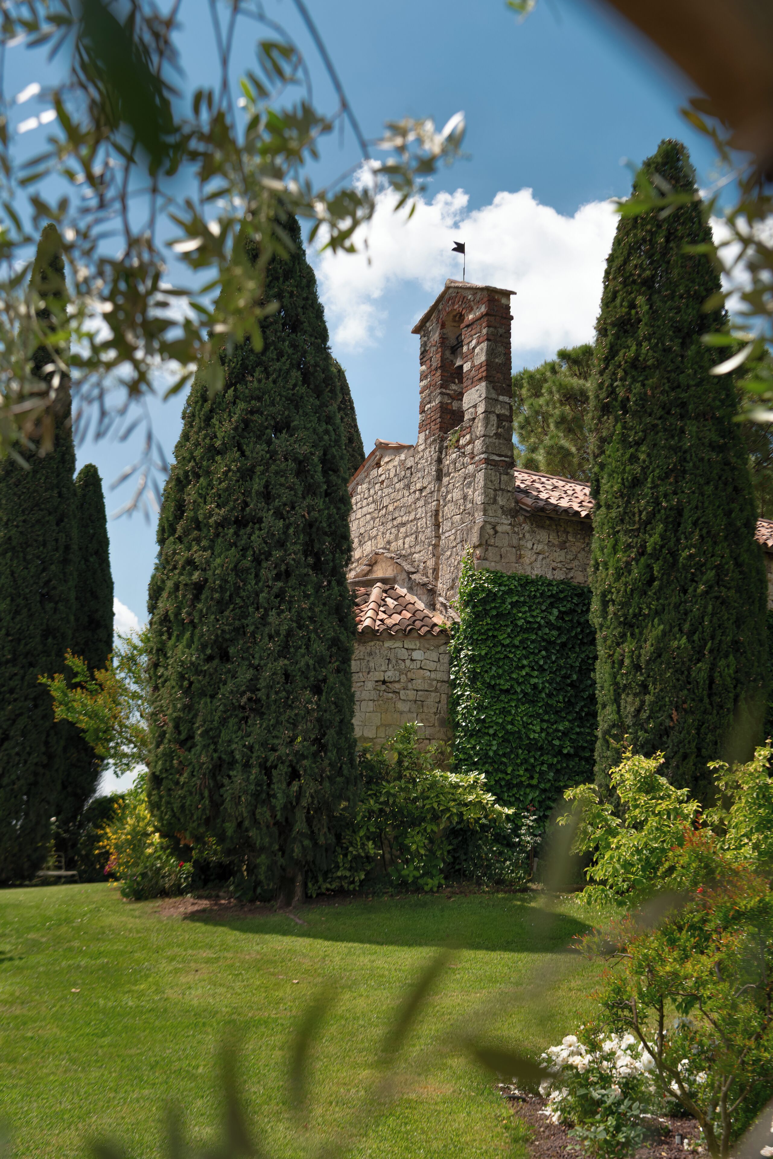 A stone building with a tower, surrounded by well-maintained greenery and a lawn.