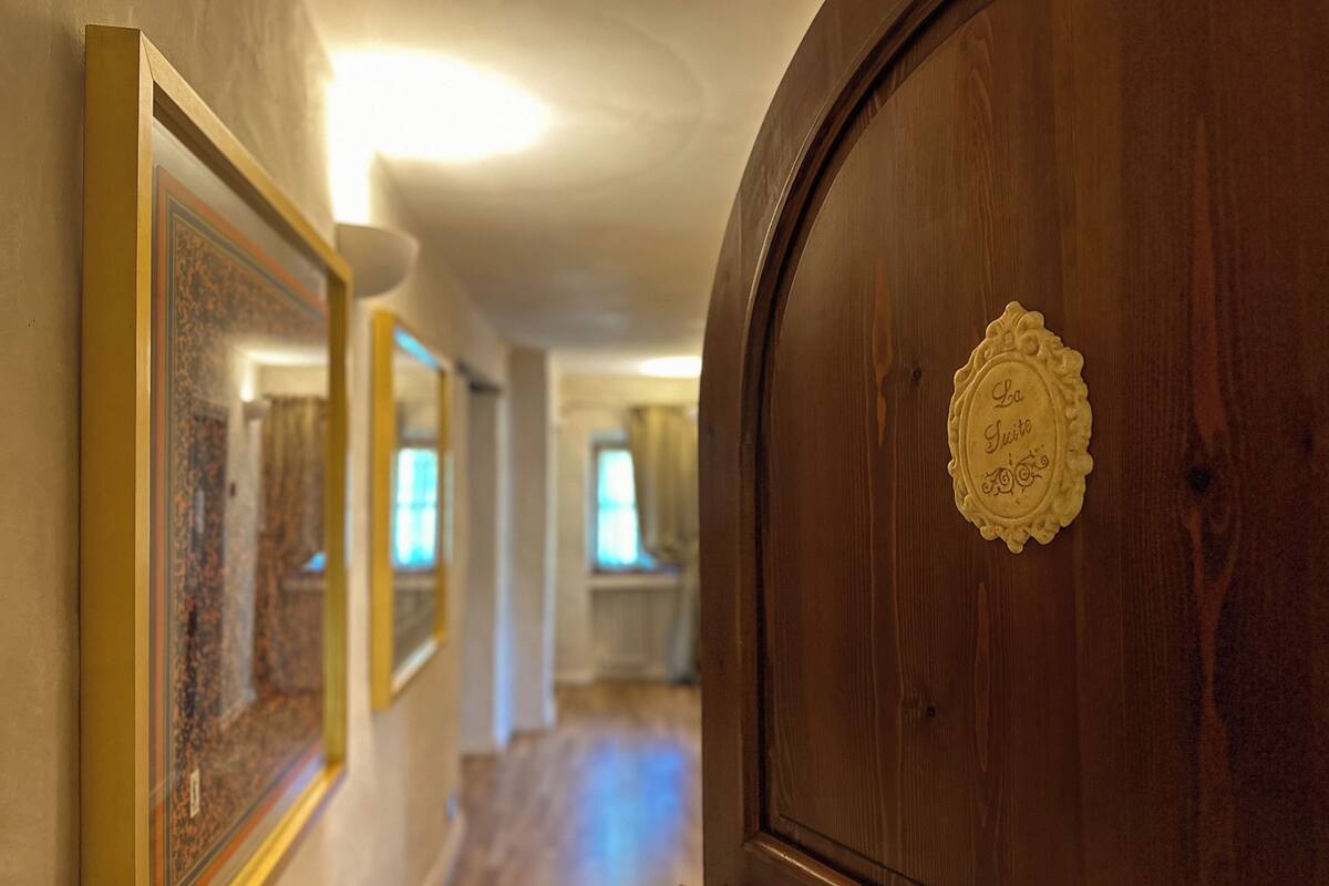 A wooden door with a plaque, a hallway with framed pictures, and a window in the background.