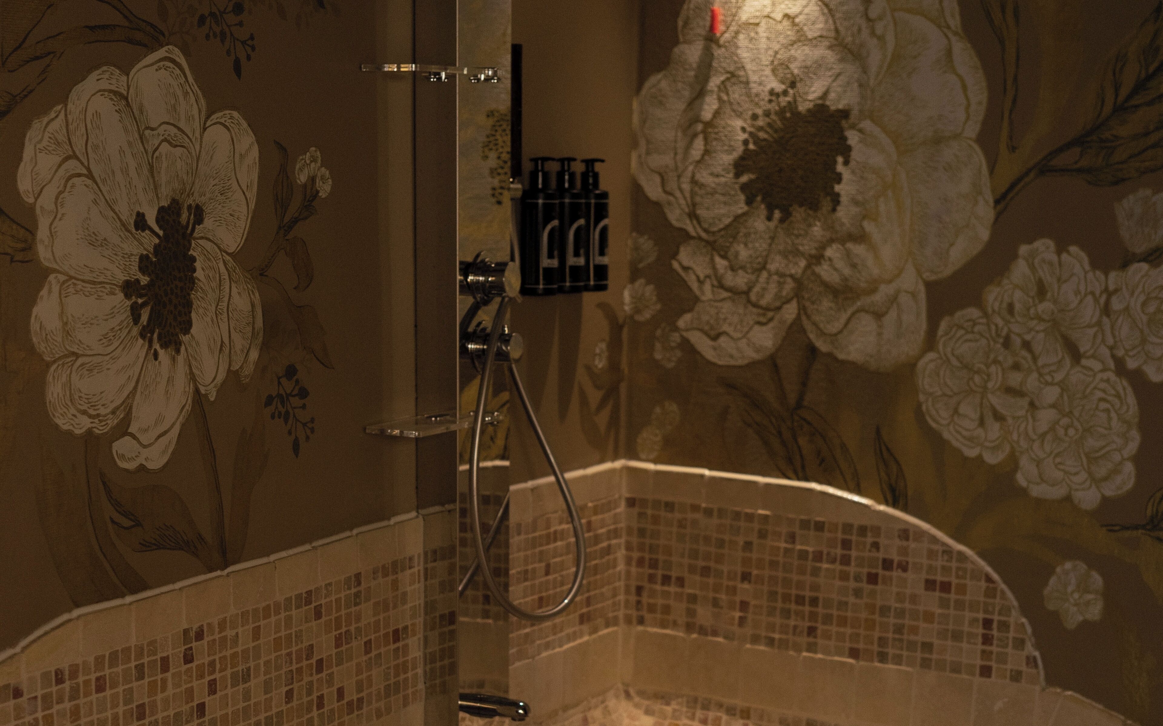 Un baño con detalles de arte floral en la pared, una ducha con cabezal de ducha de mano y suelo de baldosas.