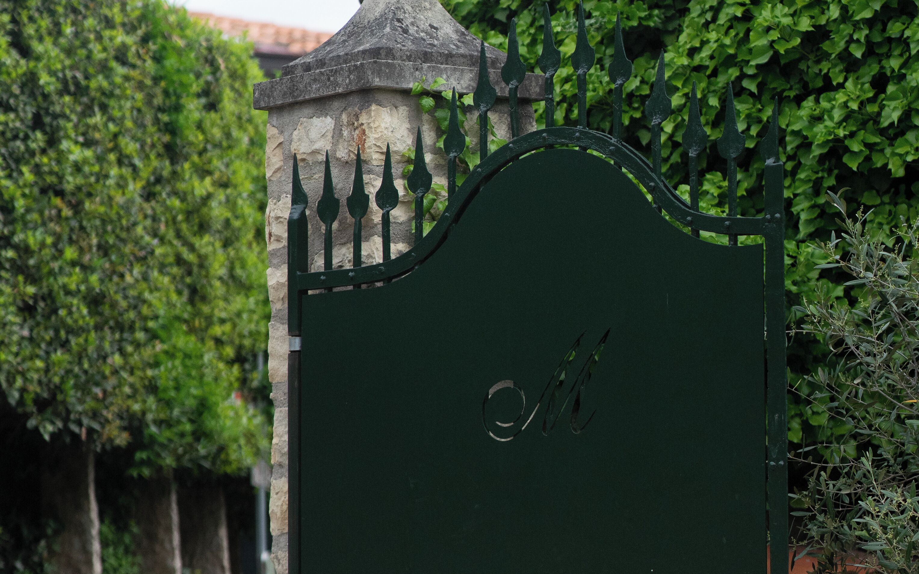 A green metal gate with a stone pillar and a stone wall covered in ivy.