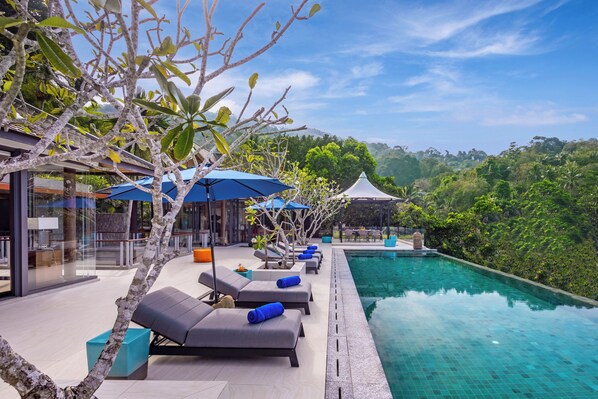 A poolside area with lounge chairs and umbrellas, surrounded by lush greenery and a clear sky. - Villa La Thalé (Kamala)