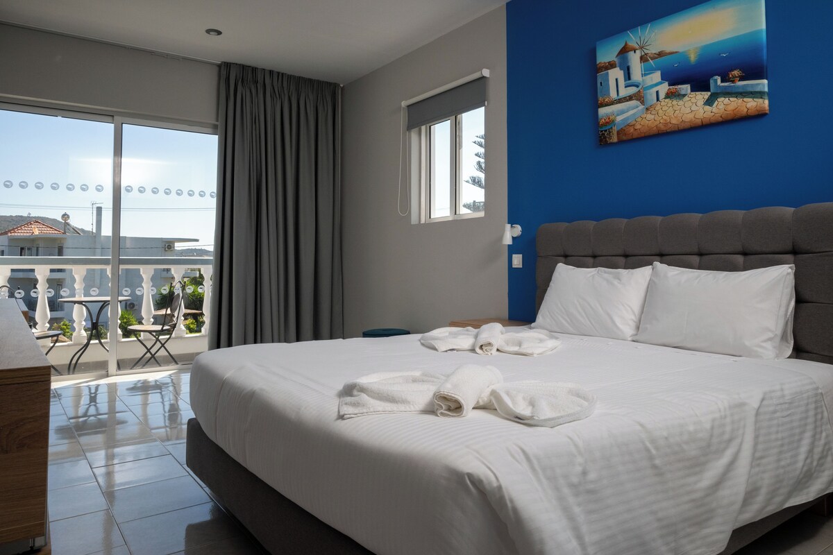 A hotel room with a large bed, a view of the city, and a painting on the wall.