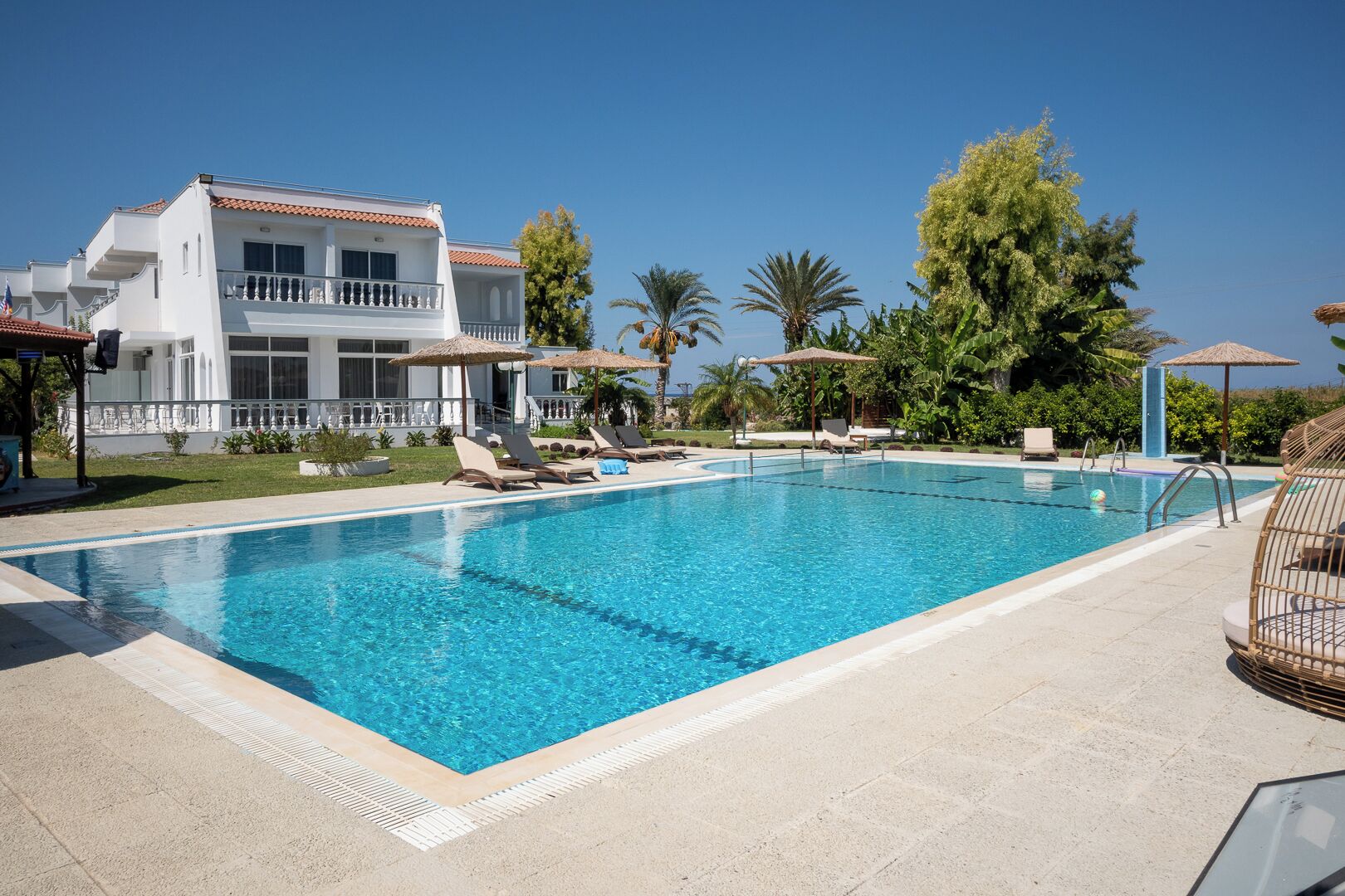 Una piscina con sillas de descanso, un edificio con balcones y vegetación tropical.