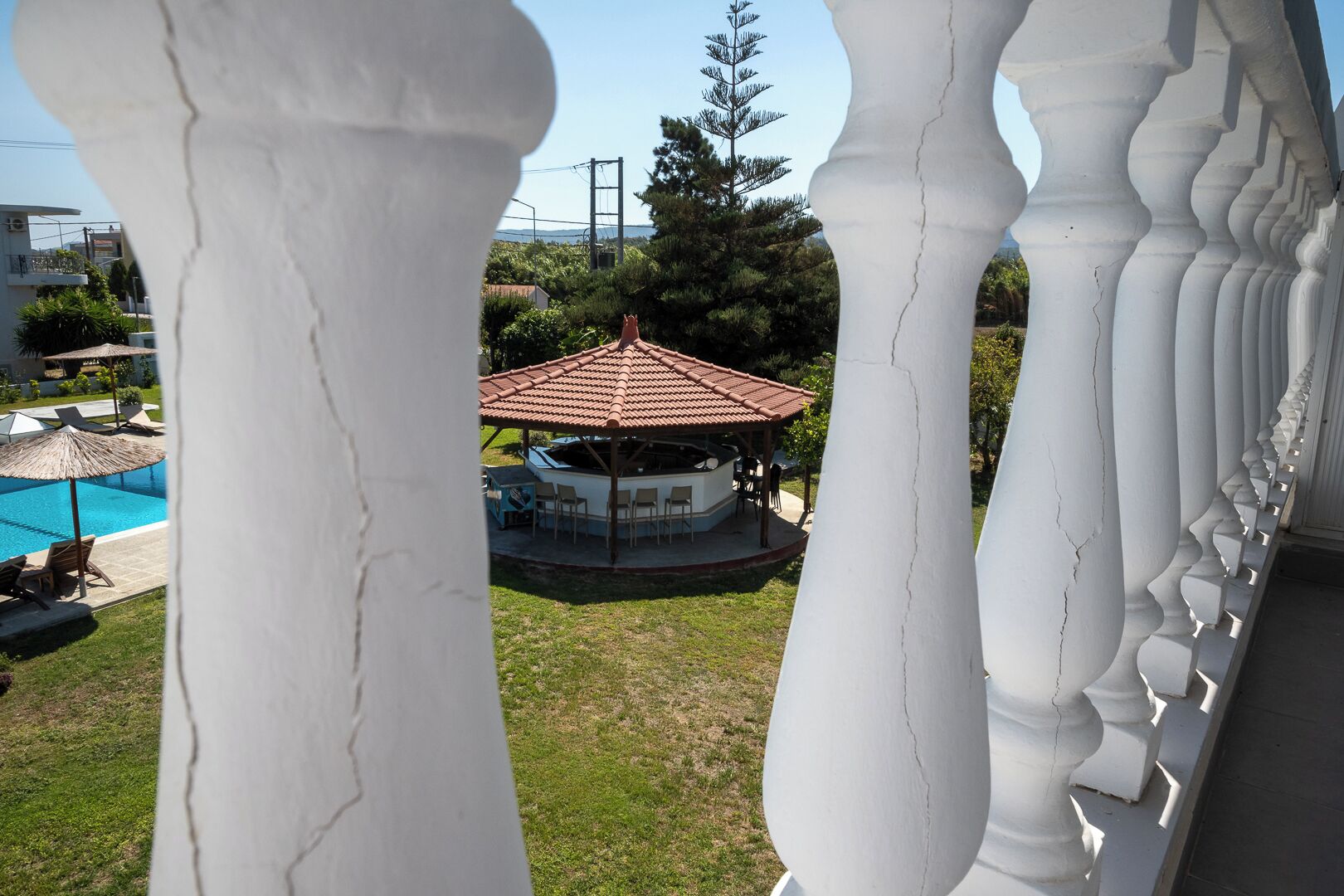 A gazebo with a tiled roof, surrounded by a pool and lounge chairs.