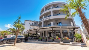 A modern hotel with a curved facade, outdoor seating area, and palm trees. - Hotel Kroi (Ksamil)
