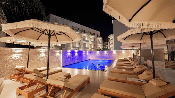 A poolside area with lounge chairs and umbrellas, a pool, and a building in the background. - Hotel Kroi (Ksamil)