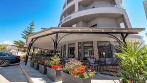 A hotel with a covered outdoor seating area, multiple floors, and a sign reading "HOTEL KROI". - Hotel Kroi (Ksamil)