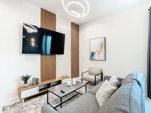Una sala de estar moderna con un televisor de pantalla plana montado en la pared, un sofá, una mesa de centro y una mesita de noche con objetos decorativos.