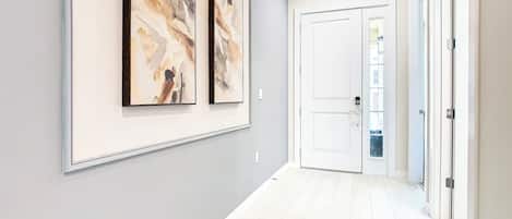 Un pasillo con dos cuadros abstractos enmarcados, una puerta blanca y un suelo blanco.