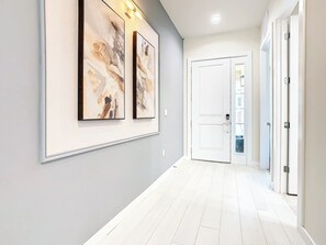 A hallway with two framed abstract paintings, a white door, and a white floor.