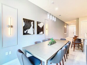 A modern dining area with a long table, chairs, and wall-mounted light fixtures.