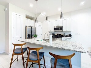 Una cocina moderna con una isla central, electrodomésticos de acero inoxidable e iluminación colgante.