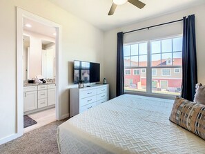 Une chambre à coucher comprenant un lit, une télévision, une commode et une fenêtre donnant sur des immeubles.