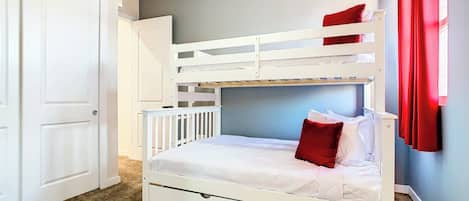 A bunk bed with a lower bunk and a single bed, white bedding, a red pillow, a door, and a carpeted floor.