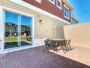 A patio with a table and chairs, a sliding glass door, and a brick floor.