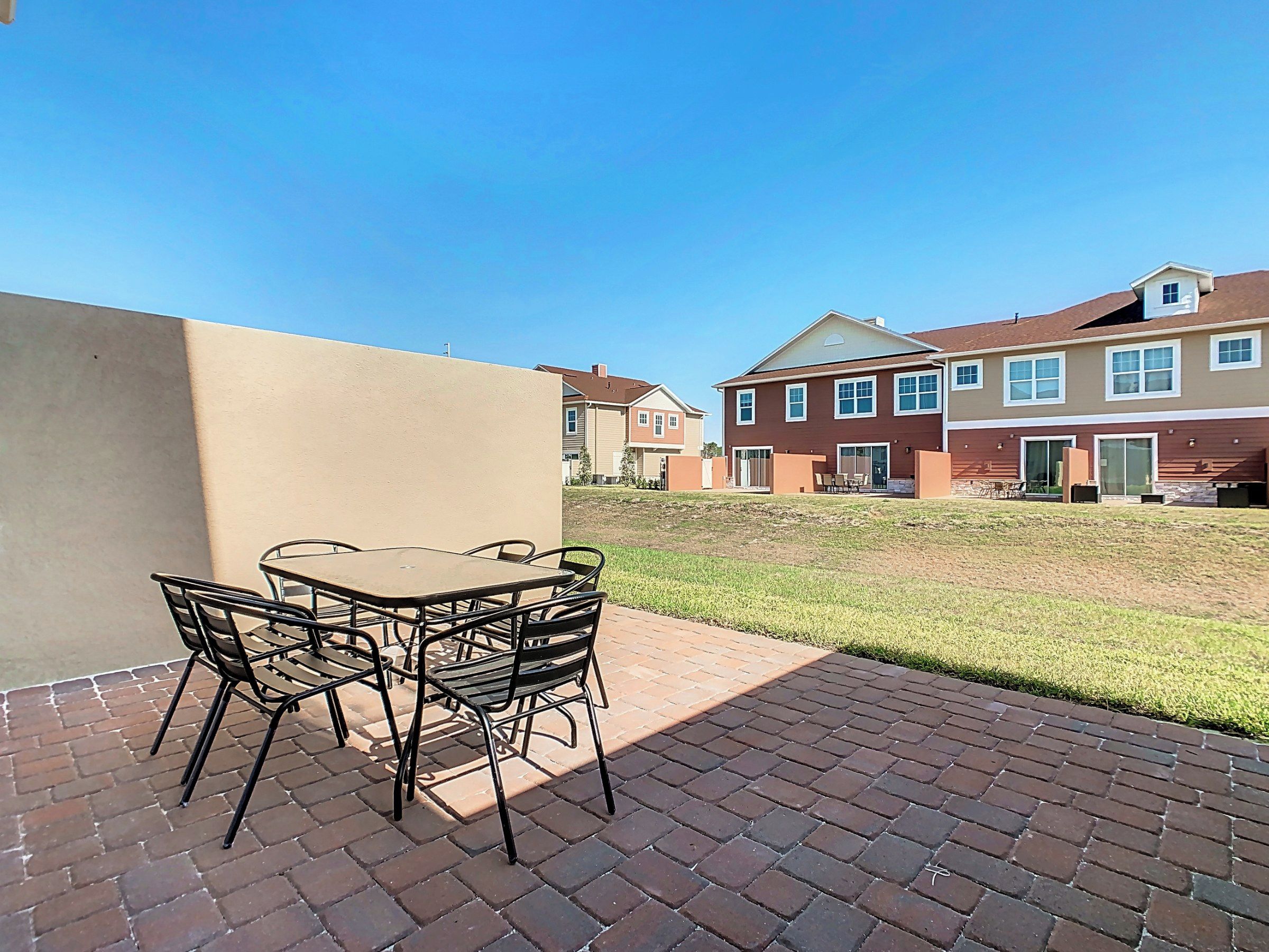 A patio area with a table and chairs, a brick pathway, and a building with multiple windows and a door.