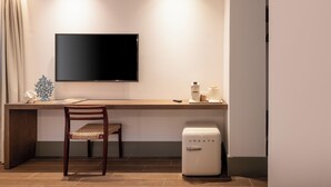 Een moderne hotelkamer met een grote flatscreen televisie aan de muur, een houten bureau met stoel, en een compacte witte minibars.