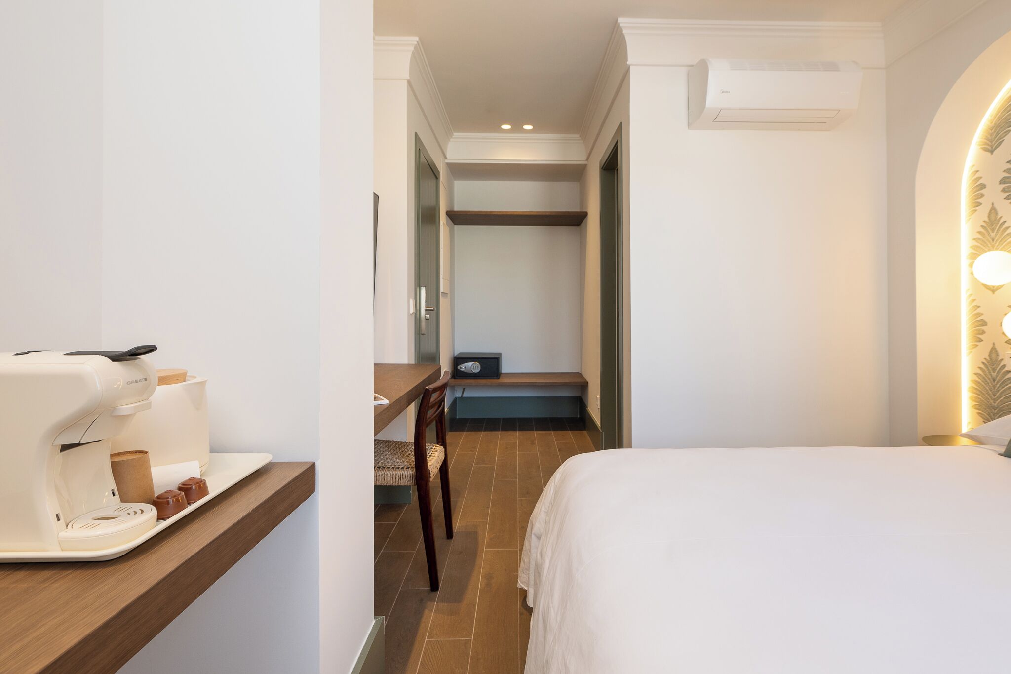 A hotel room with a bed, a desk with a coffee maker, a chair, and a small table with a tray.