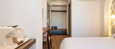 A hotel room with a bed, a desk with a coffee maker, a chair, and a small table with a tray.