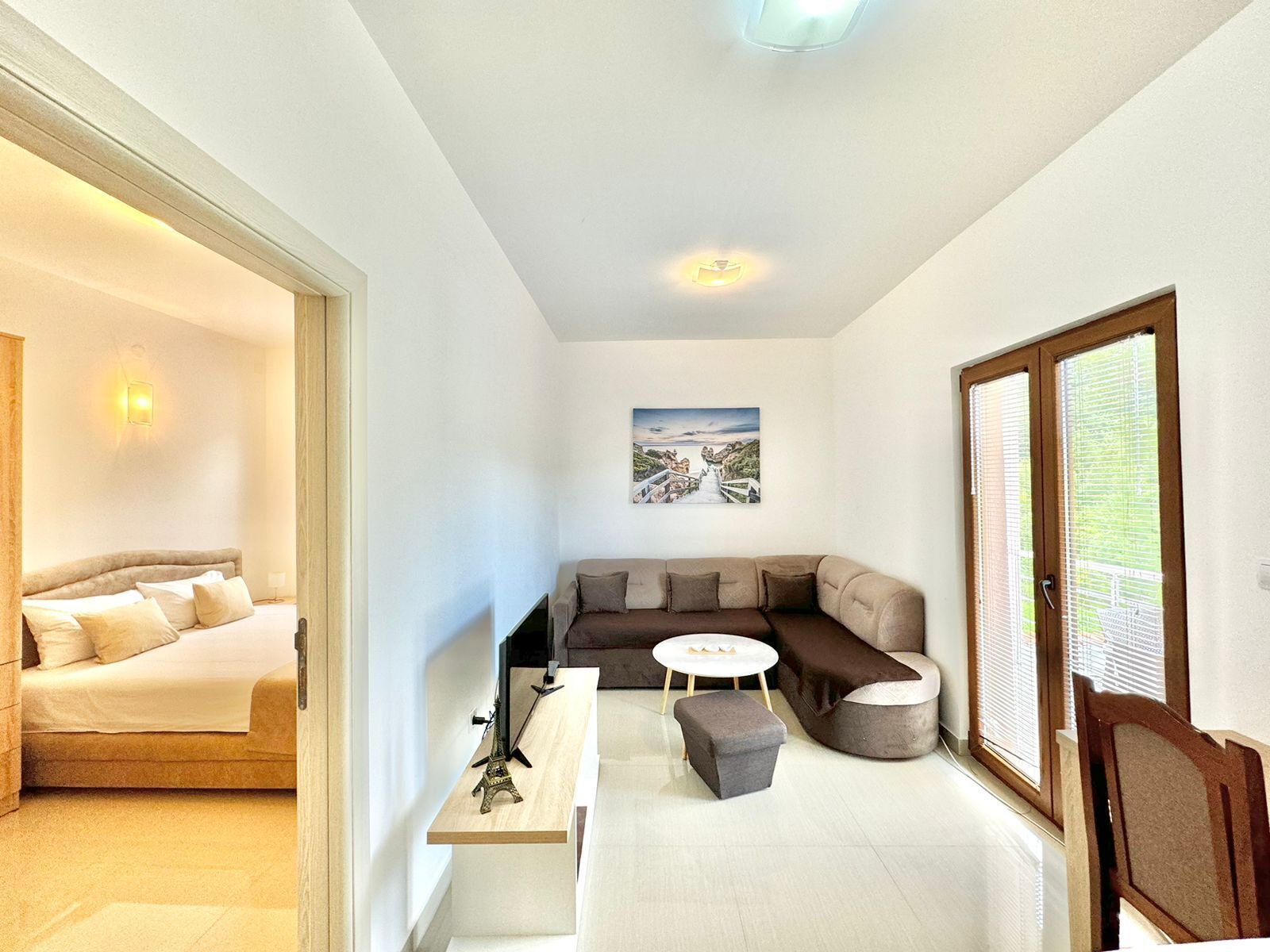 A modern living room with a sofa, a small round table, and a bed in the adjacent room.