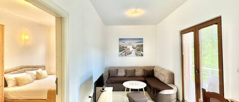 A modern living room with a sofa, a small round table, and a bed in the adjacent room.