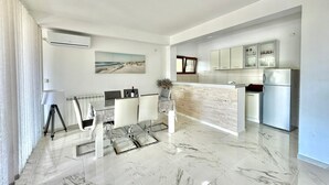 A modern kitchen with a marble countertop, a built-in fridge, and a dining area with a glass table and chairs. - Stars Residence (Petrovac)
