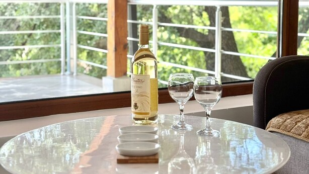 A round glass table with a bottle of white wine and two glasses, set on a balcony with a view of trees. - Stars Residence (Petrovac)